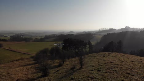 Aerial-view-of-beautiful-green-hills-with-trees-and-lakes,-moving-toward-the-sunset-in-Odsherred,-Denmark