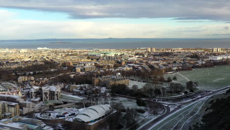 Toma-Aérea-De-Edimburgo-En-La-Nieve-Con-El-Palacio-De-Holyrood-En-La-Distancia-En-Un-Día-Soleado-De-Invierno-Crips