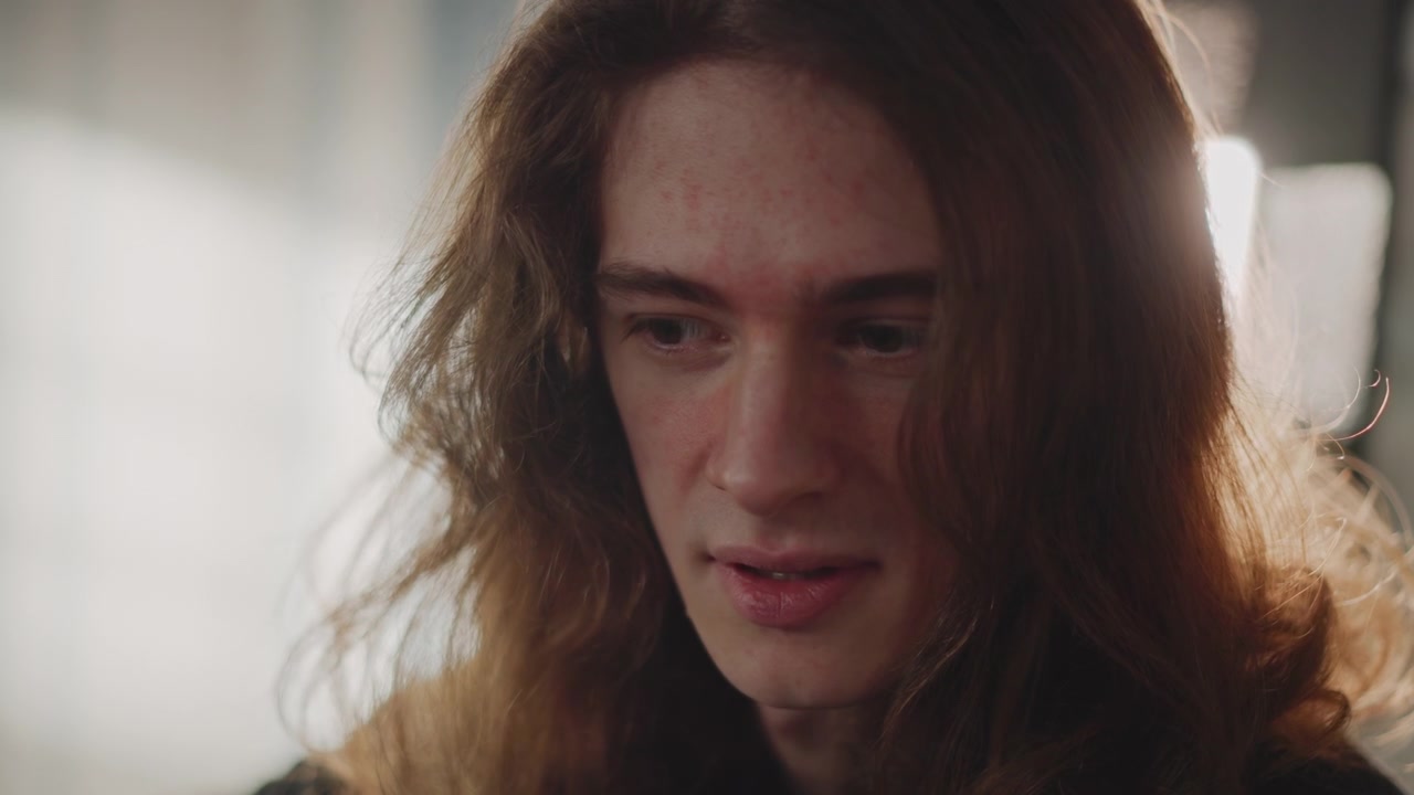 Young white male guitarist practicing guitar, intimate sunlit music school session, long hair, close portrait shots, finger movement on strings, focused expression, teacher observing offscreen, warm