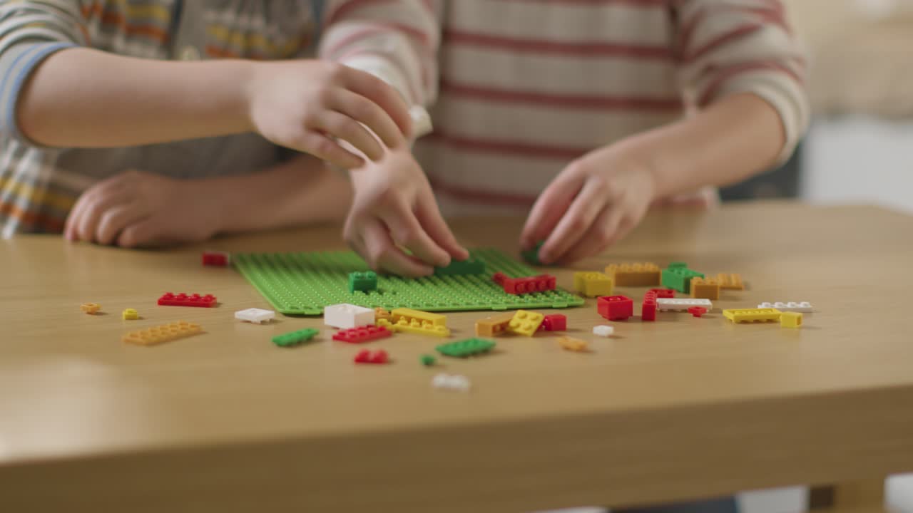 집에서 테이블 위에 플라스틱 건축 벽돌로 놀고 있는 두 아이의 가까운 모습