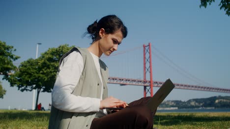 mujer trabajando en una computadora portátil en un parque junto al puente