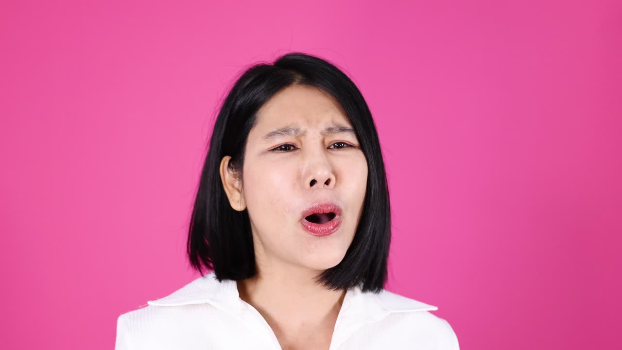 흰색 셔츠를 입은 여성이 슬픔과 좌절감을 표현하고, 감정적인 반응을 보입니다. 스튜디오 조명, 핑크색 배경입니다.
