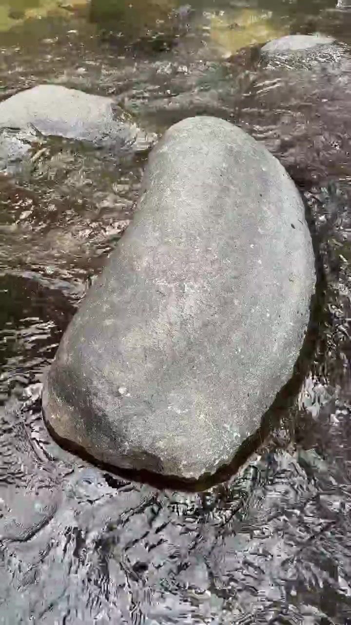 Acqua limpida che scorre attorno a una grande roccia liscia di fiume.