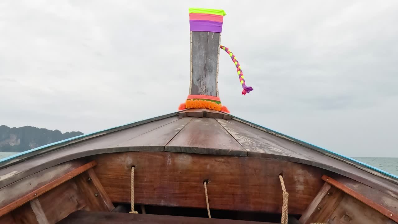 A vibrant long tail boat glides through the ocean, showcasing its colorful bow against a cloudy sky.