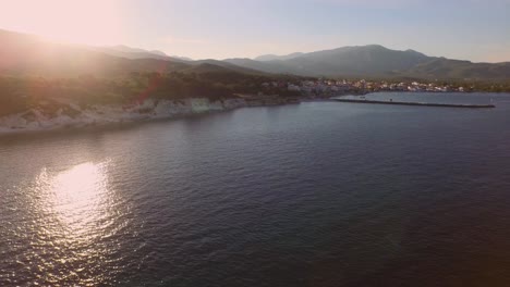 Aerial:-Small-fishing-town-with-Greek-flag-on-Samos-island,-Greece