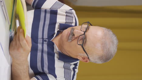 Vertical-video-of-Home-office-worker-old-man-reading-a-book.