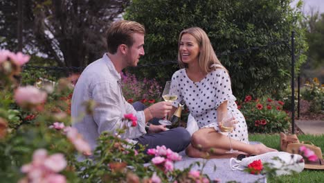 couple sharing a laugh as they share a rose garden picnic together and sip champagne