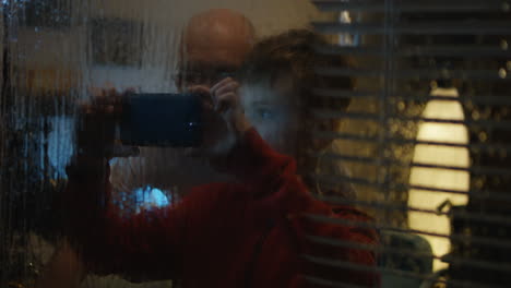 a boy and his father take pictures at night through a rainy window