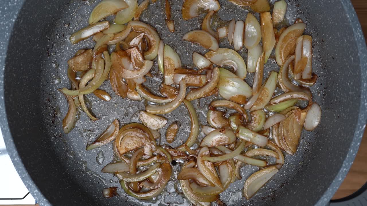 top down shot of white onion pieces frying and caramelizing in a large frying pan