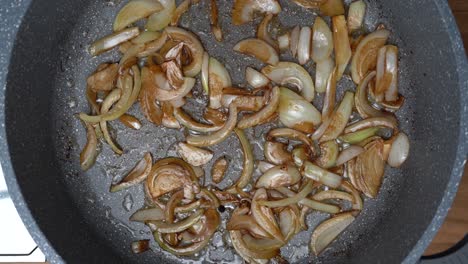 top down shot of white onion pieces frying and caramelizing in a large frying pan