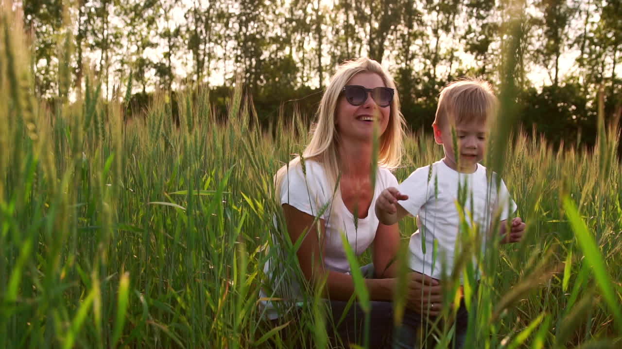 Liebende Mutter und Sohn umarmen sich und spielen mit einem Fußball auf einem Feld mit Ähren im wunderschönen Sonnenuntergangslicht in weißen T-Shirts