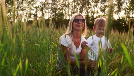 loving mom and son hugging and playing with a soccer ball in a field with spikelets in beautiful sunset light in white t-shirts