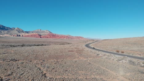 aerial drone shot of red rock scenic highway with mountains in the background