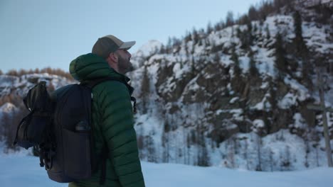 Young-male-hiker-in-winter-mountains-stops-and-removes-hood-of-jacket-to-admire-view