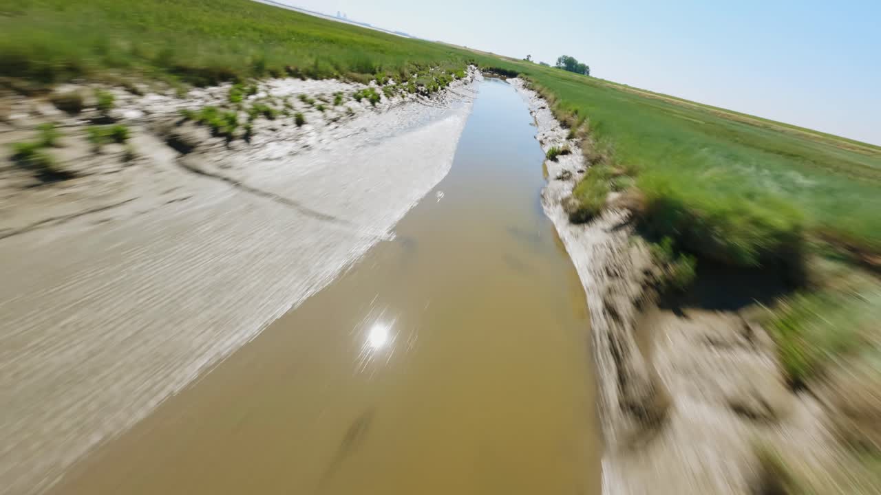 푸른 여름 하늘 아래 녹색 습지를 통해 진흙 투성이 도랑을 따라 화려한 고속 fpv 드론 샷