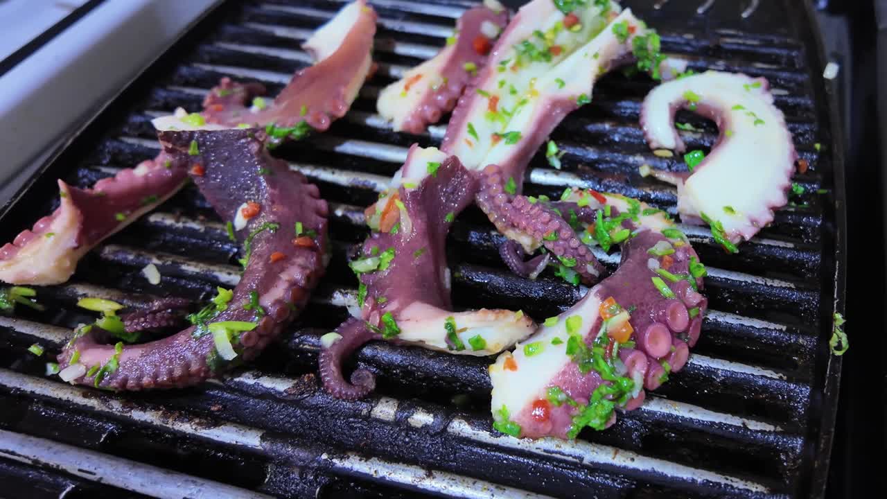 Pieces of grilled octopus tentacles, seasoned with chopped herbs and spices, cooking on a hot grill pan. Texture octopus and the charred grill marks highlight