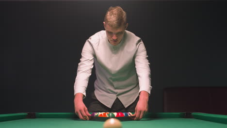 close-up of billiards trainee in shirt intensely focused on pool table as he prepares to break. his hands hover over rack of colorful balls on vibrant green felt, soft light against dark background