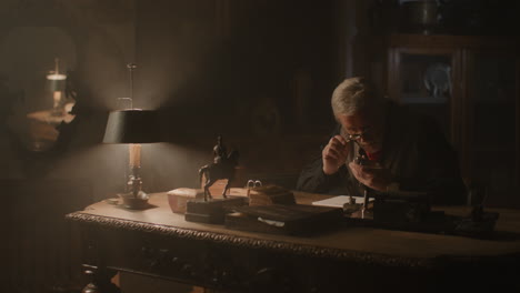 older passionate man evaluates an old silver skull watch in his office at night