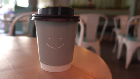 a close-up of a coffee cup with a smiley face on it, sitting on a table in a cafe.