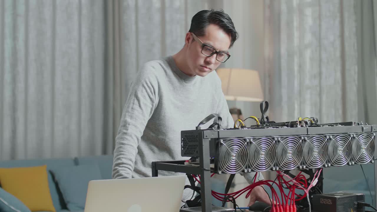 안경을 쓴 아시아인 남자가 노트북으로 일하면서 암호화폐 채굴을 보고 있다