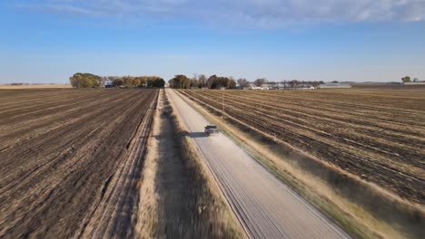 Luftdrohne-Nach-Aufnahme-Eines-Pickup-Trucks,-Der-Auf-Einer-Staubigen-Schotterstraße-Unter-Blauem-Himmel-Im-Ländlichen-Mittelwesten-Von-Iowa-Fährt