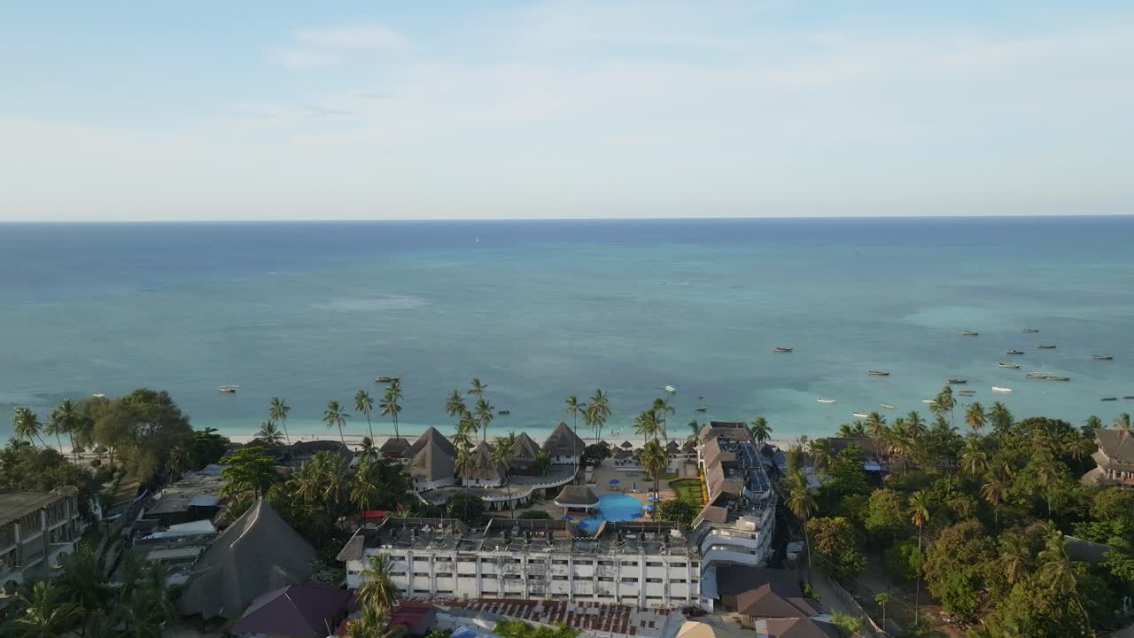 Volo cinematografico con drone sopra resort di spiagge tropicali che rivela Nungwi Beach a Zanzibar. Sabbia bianca, acqua turchese e paesaggi costieri di lusso creano una scena di viaggio vivace e invitante