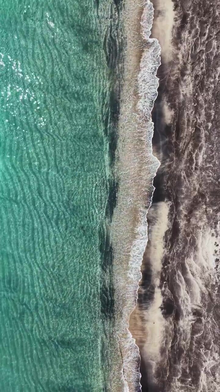 Onde che si infrangono sulla riva di una spiaggia con acqua limpida e litorale sabbioso di giorno.