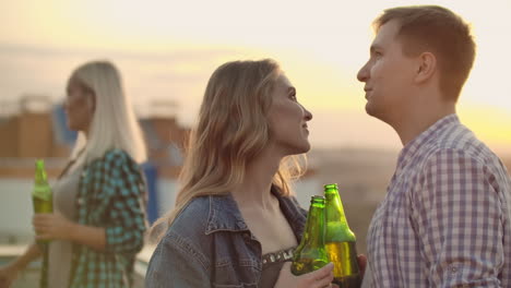 two young couples with beer talking to each other on the roof. they enjoy moments with their halves and look into each other's eyes.