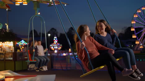 two young women enjoying a swing ride at a night amusement park