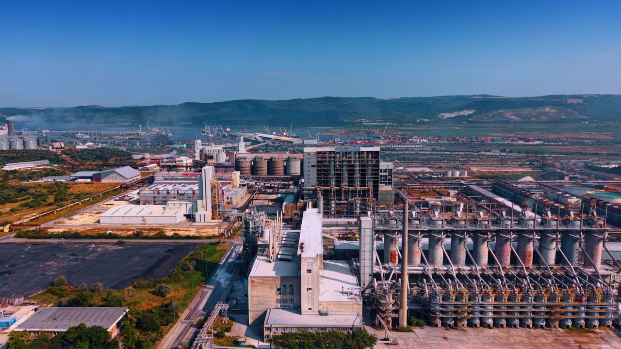 Instalação de processamento com silos e infraestrutura portuária. Uma vista elevada mostra silos cilíndricos, estruturas de aço e transportadores que se estendem em direção a um terminal de carga costeiro.