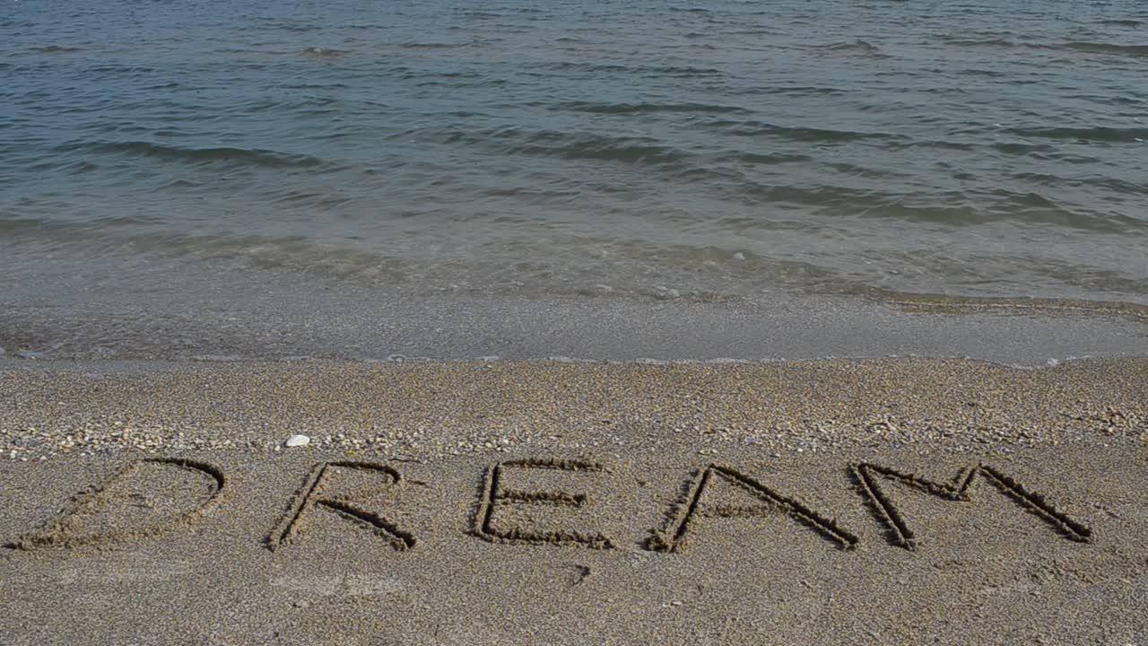 Inscription Dream on sea beach sand, with the wave. Shooting on the beach