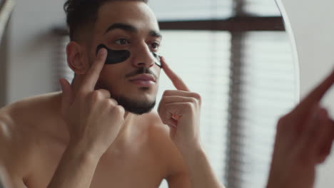 hombre aplicando parches en los ojos frente al espejo