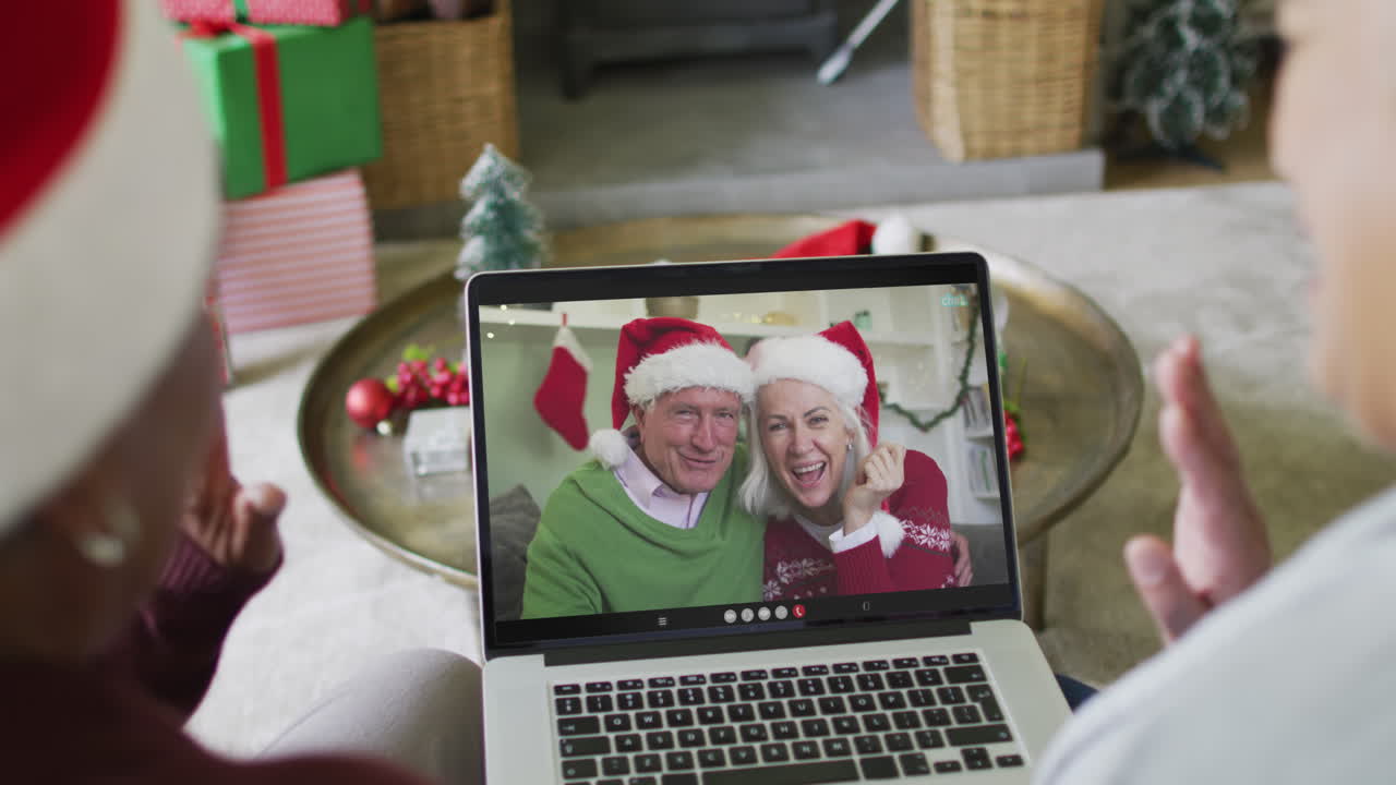 diversas amigas mayores que usan una computadora portátil para una videollamada de navidad con una pareja feliz en la pantalla