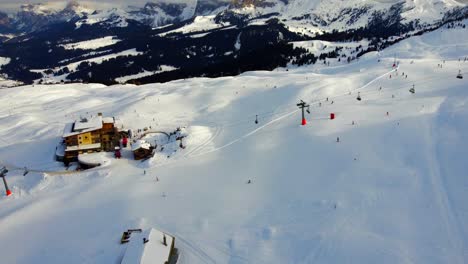 Flying-over-a-ski-slope-in-Alpe-di-Siusi-during-winter-with-a-slow-pan-up-which-reveals-the-Sassolungo-located-in-the-background