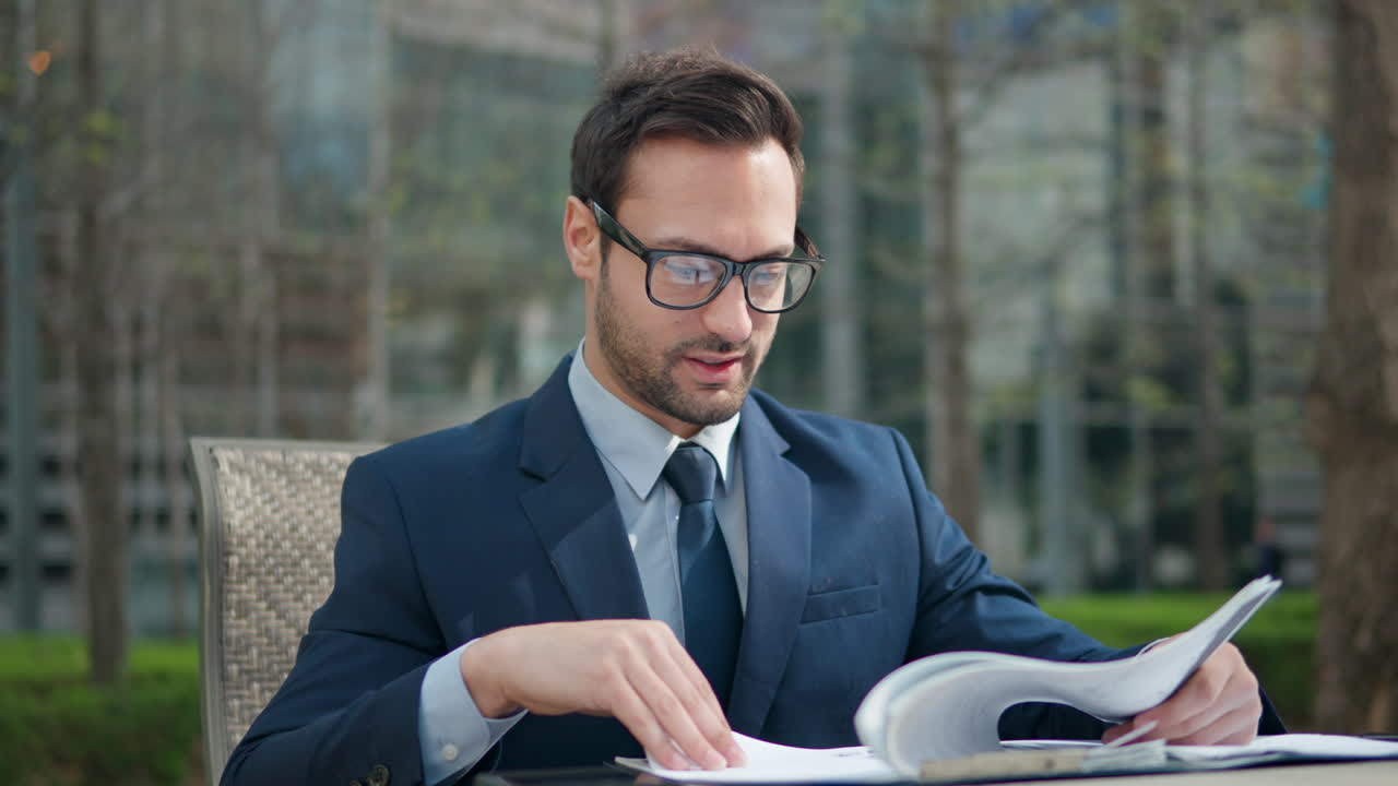 Working Outdoors Concept, Professional business man in suit working with papers turning pages and using mobile phone sitting in a park outdoors