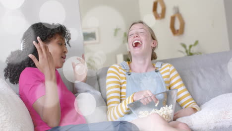 animation of white light spots over two diverse teenage girls laughing and playing with popcorn