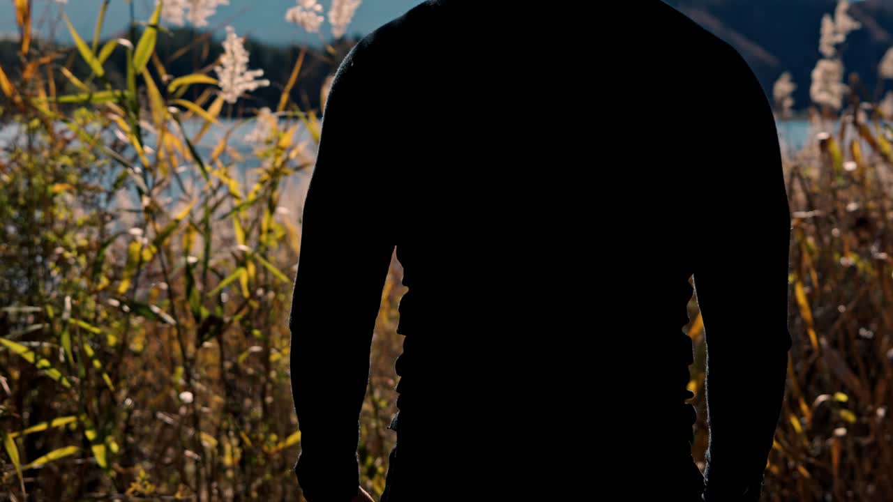 A cinematic shot of a man standing in awe, gazing at the majestic snow-covered Mt. Fuji in the background, framed by vibrant red autumn foliage.