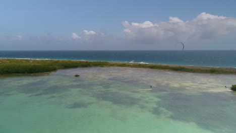 grupo de personas cabalgando y deslizándose por el agua sosteniendo una gran cometa controlada a mano impulsada por el viento