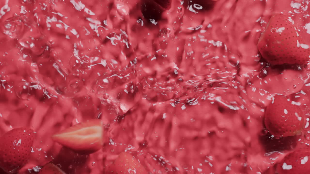 Video of strawberries falling into water with copy space on red background