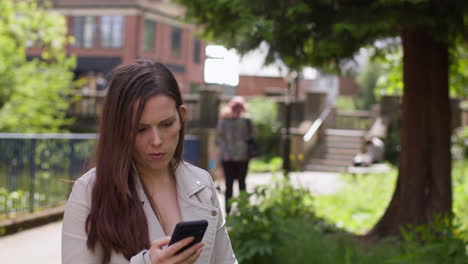mujer estresada y preocupada al aire libre con preocupaciones financieras sobre el costo de la vida crisis de la deuda y el pago de facturas mirando el teléfono móvil en el parque de la ciudad