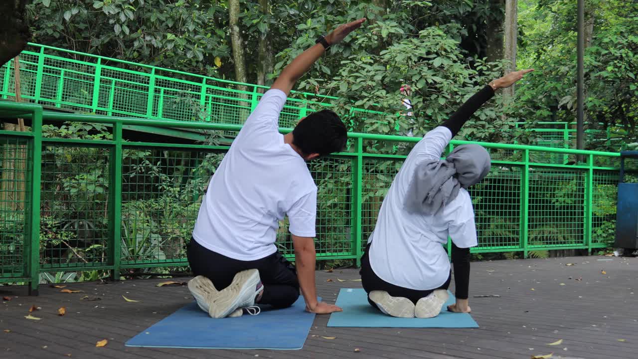 Back view of healthy couple doing yoga practice on yoga mat at the greenery park