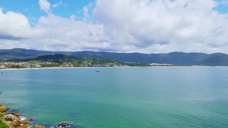 Luftaufnahme-Eines-Strandufers-Mit-Kleinen-Booten,-Bergen,-Viel-Grünfläche,-An-Einem-Sonnigen-Tag