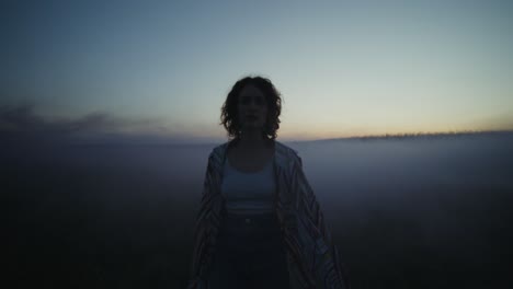 woman walking through foggy field at dusk
