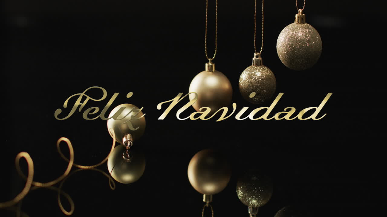 Feliz navidad text in gold over old christmas baubles on black background