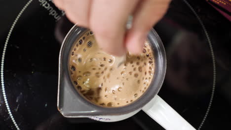 stirring fresh coffee with a spoon in the coffee pot on the stove after adding fresh coffee