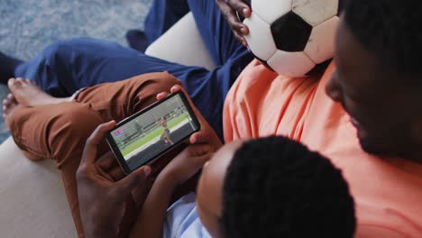 composite of father and son at home watching athletics high jump event on smartphone