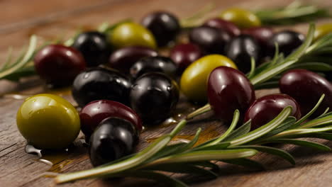 assortment of olives and rosemary sprigs on a wooden background
