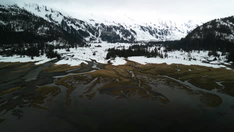 Drone-circling-in-front-of-marshlands-and-snowy-mountains-in-cloudy-Alaska