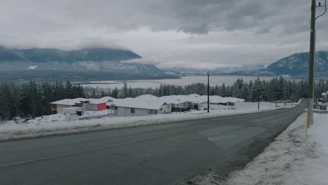 Toma-Panorámica-De-Un-Barrio-Residencial-En-Invierno-Con-Un-Lago-Y-Montañas-Al-Fondo