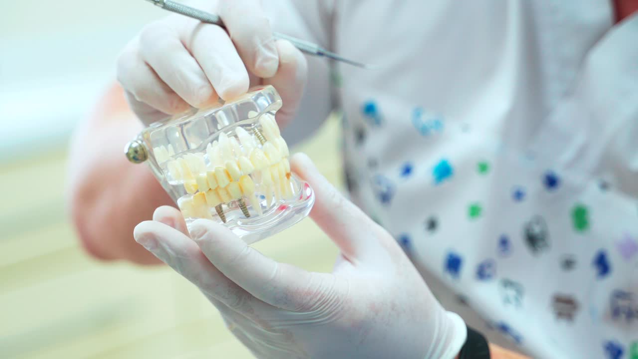 A doctor in white rubber gloves removes a denture from a jaw layout. Training of dentists on a model of teeth